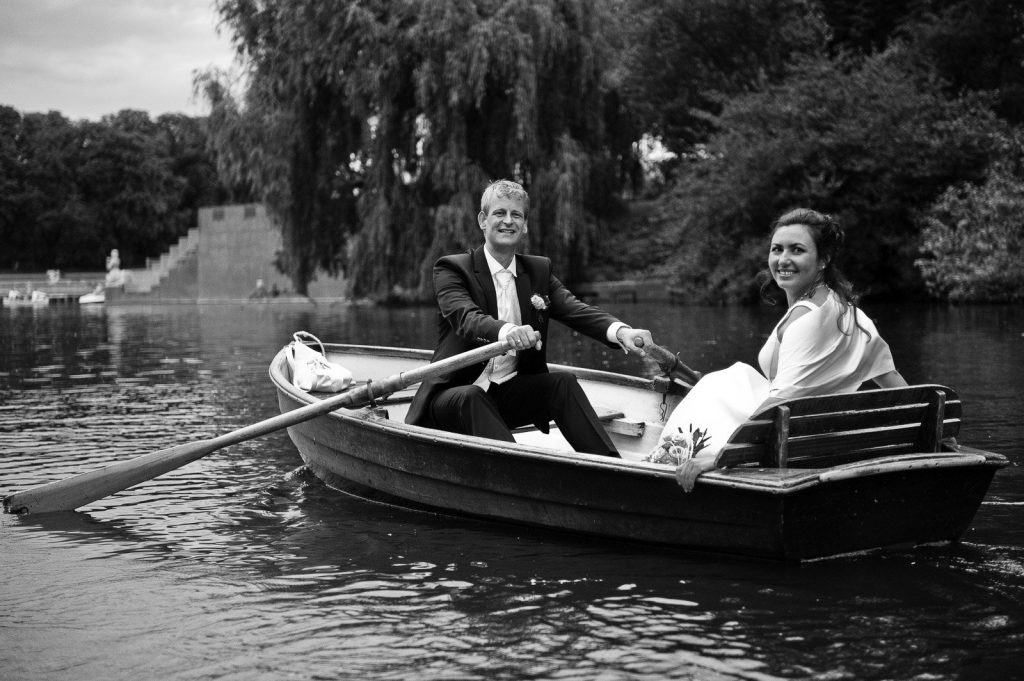 Lachendes Hochzeitspaar im romantischen Ruderboot auf dem Stadtparksee in Hamburg Winterhude bei den Brautpaarfotos beim Hochzeitsfotograf Hamburg