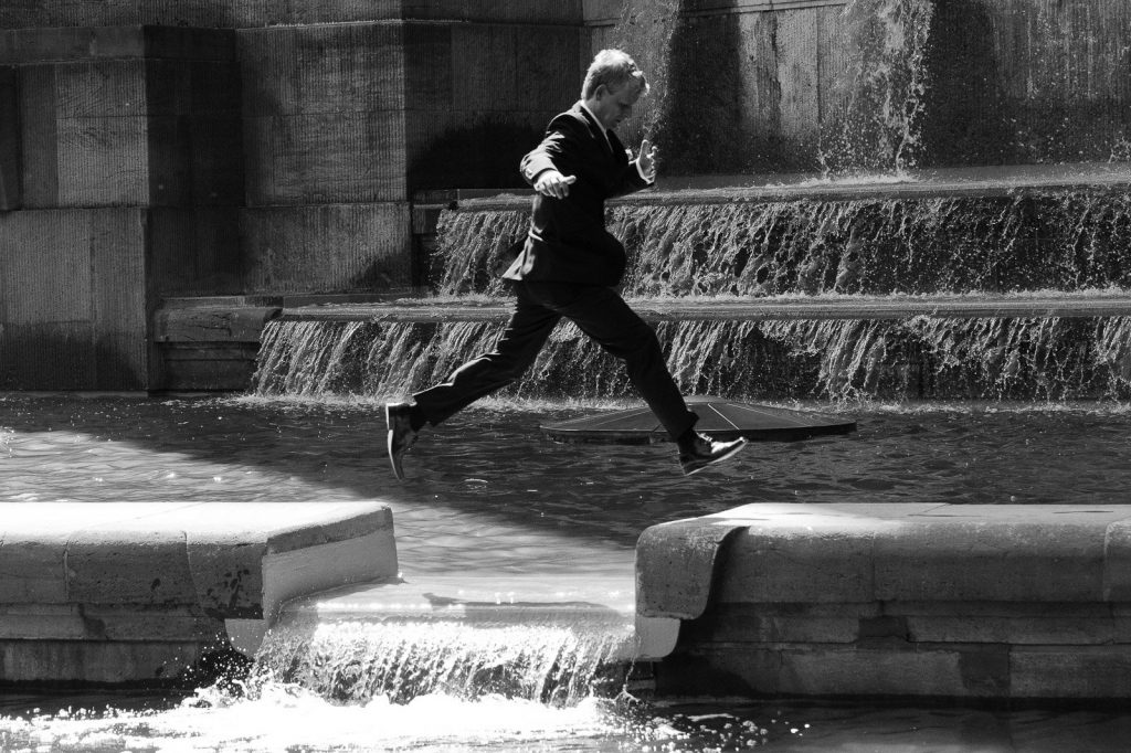 Bräutigam springt über das Wasser am Springbrunnen vor dem Planetarium im Hamburger Stadtpark bei den Brautpaarfotos beim Hochzeitsfotograf Hamburg