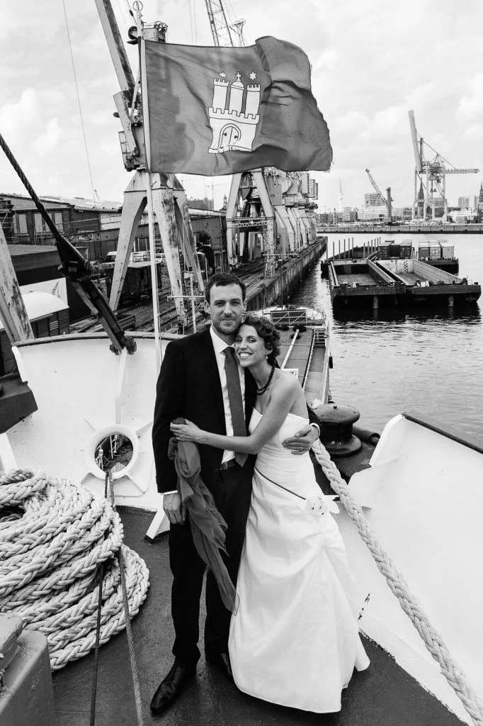 Hochzeitspaar posiert am Bug des historischen Frachters MS Bleichen vor der Flagge Hamburgs im Titanic Style Hochzeitspaar schlendert über die Kaianlagen am Australiakai im Hamburger Hafen beim Hochzeitsshooting mit dem Hochzeitsfotograf Hamburg