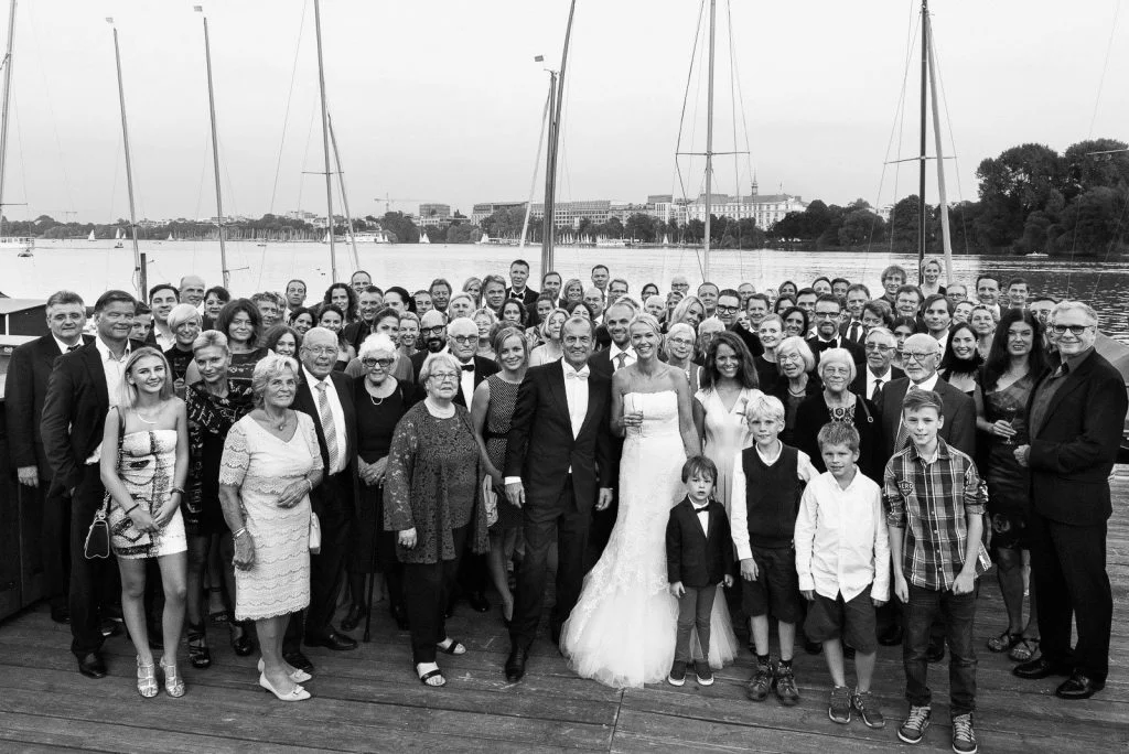 Gruppenbild der Hochzeitsgesellschaft auf dem Anleger vom Restaurante Portonovo mit Blick auf das Hotel Atlantic am Alsterufer auf der Außenalster am Rothenbaum beim Hochzeitsfotograf Hamburg