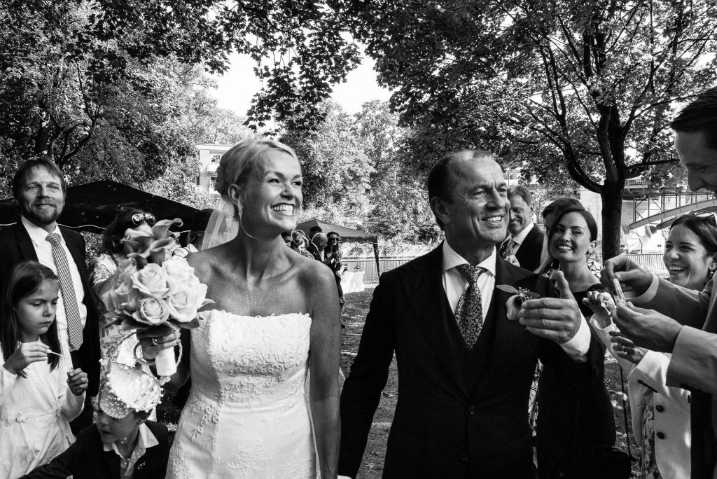Das Hochzeitspaar läuft voller Freude an seinen Hochzeitsgästen vorbei, die spalier stehen und das Brautpaar in ein Meer aus Seifenblasen eindecken im Seelemannpark an der Eppendorfer Hochzeitskirche beim Hochzeitsfotograf Hamburg