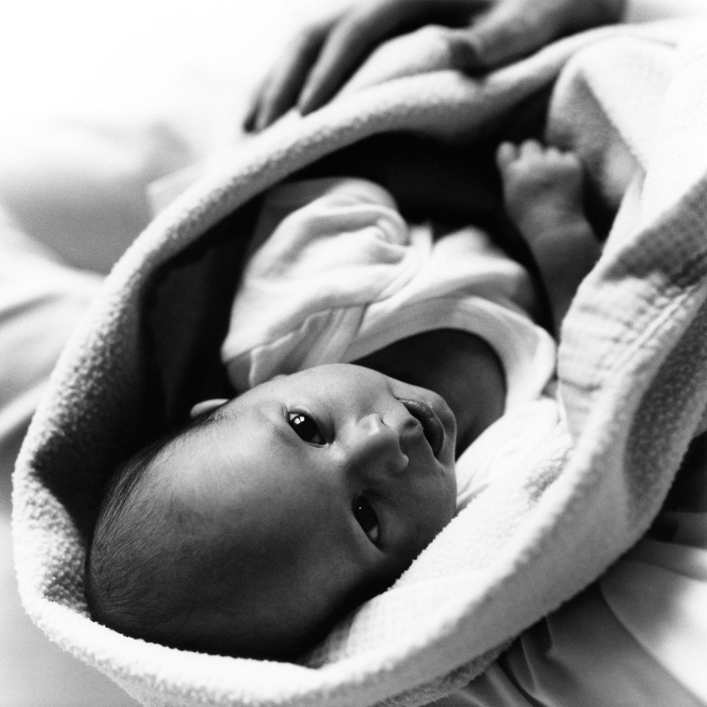 Baby liegt in der Babydecke und schaut zur Kamera bei der Neugeborenenfotografie in Hamburg Sasel
