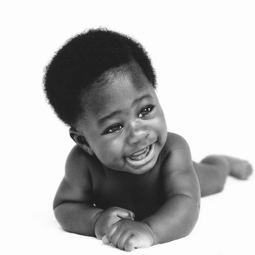 Baby liegt auf dem Bauch und laechelt in die Kamera beim Homeshooting