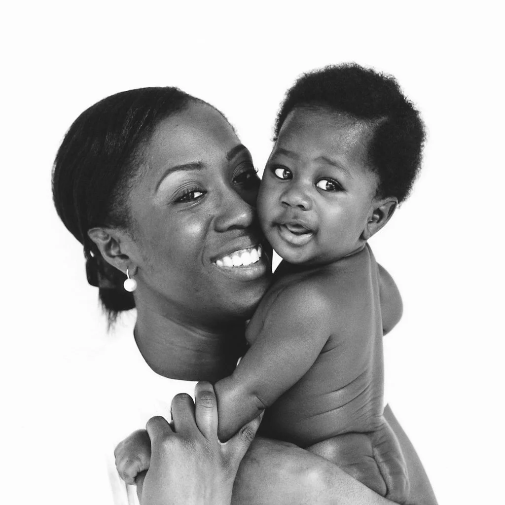 Mama kuschelt mit ihrem Baby und beide schauen in die Kamera beim Baby Fotoshooting zuhause