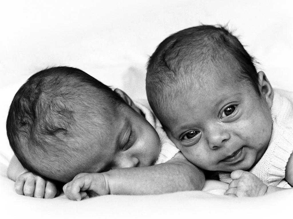 Zwillinge auf dem Bauch liegend, ein Zwillingsbaby hebt den Kopf und schaut beim Baby Fotoshooting in Hamburg Neustadt