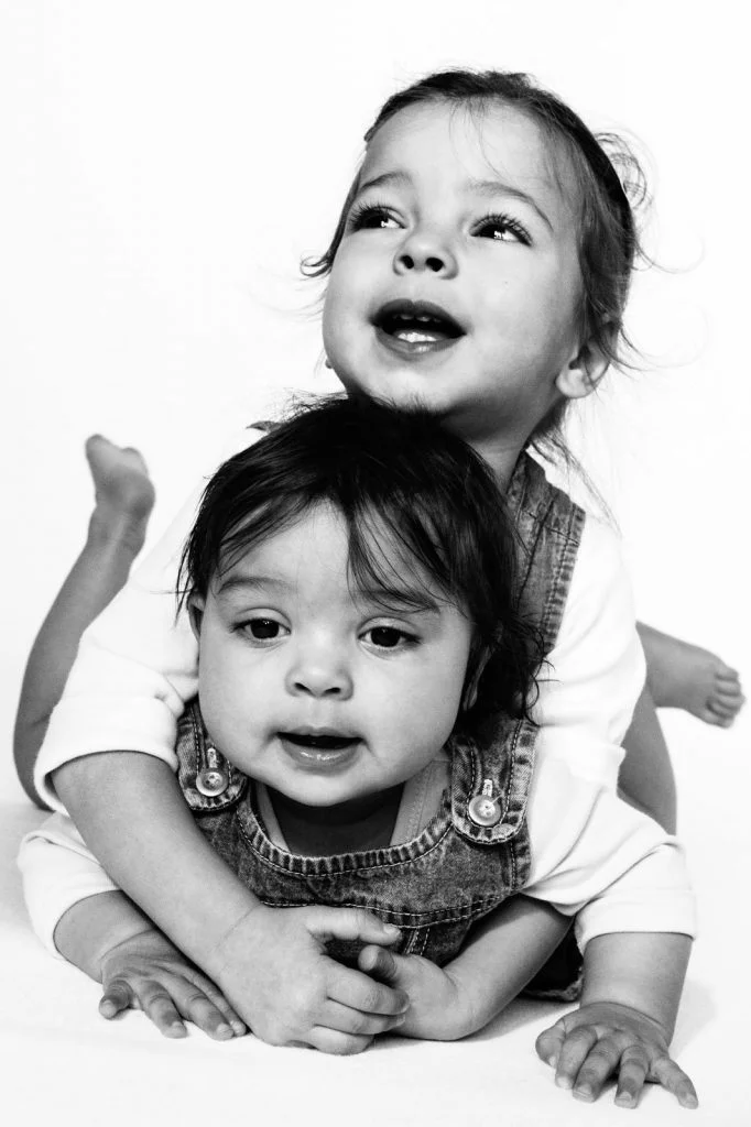 Baby und große kleine Schwester turnen gemeinsam auf der Tagesdecke beim Baby Fotoshooting zuhause in Hamburg Eppendorf