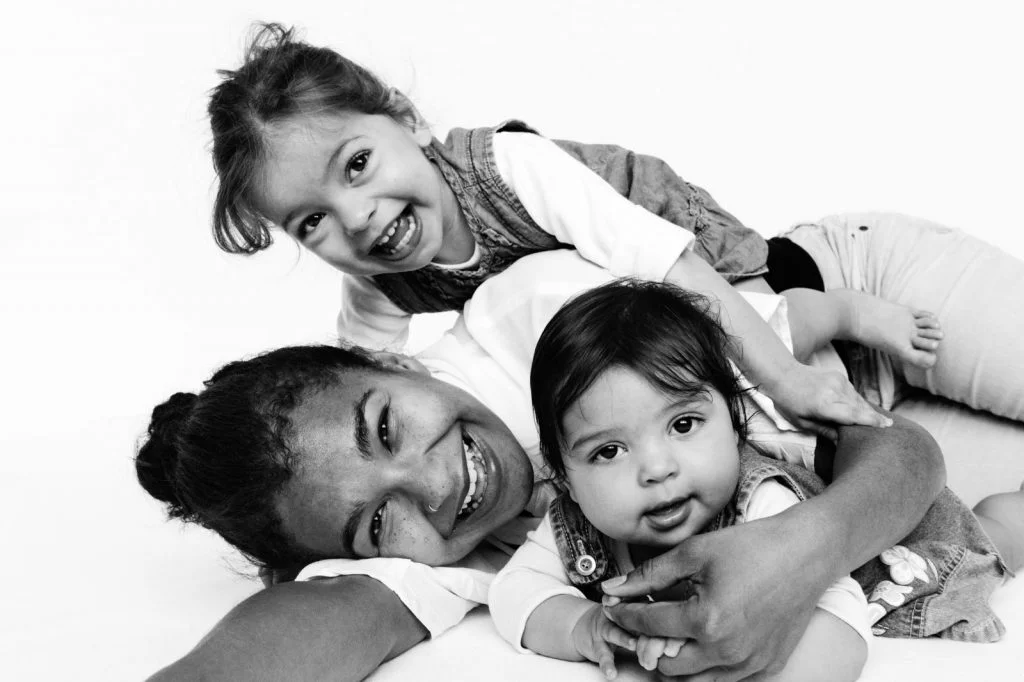 Baby, kleine Schwester und Mama liegen gemeinsam auf der Tagesdecke beim Baby Fotoshooting zuhause in Hamburg Eppendorf