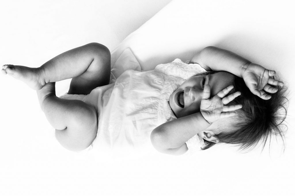 Baby lacht und hält sich die Hände vors Babygesicht beim Baby Fotoshooting zuhause in Hamburg