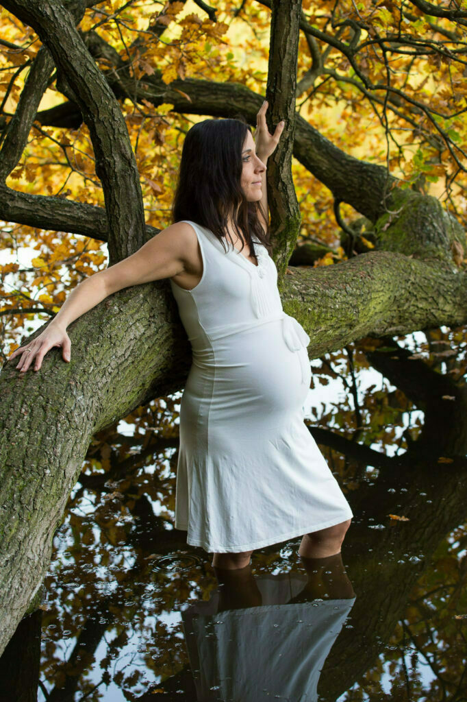 Schwangere im Wasser am Baum mit Herbstlaub bei den Babybauchfotos in Hamburg am See in der Natur