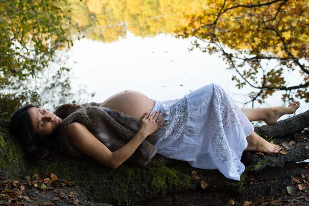 Schwangere liegt am Seeufer mit ihren Händen auf dem Babybauch bei den Babybauchfotos in Hamburg in der Natur
