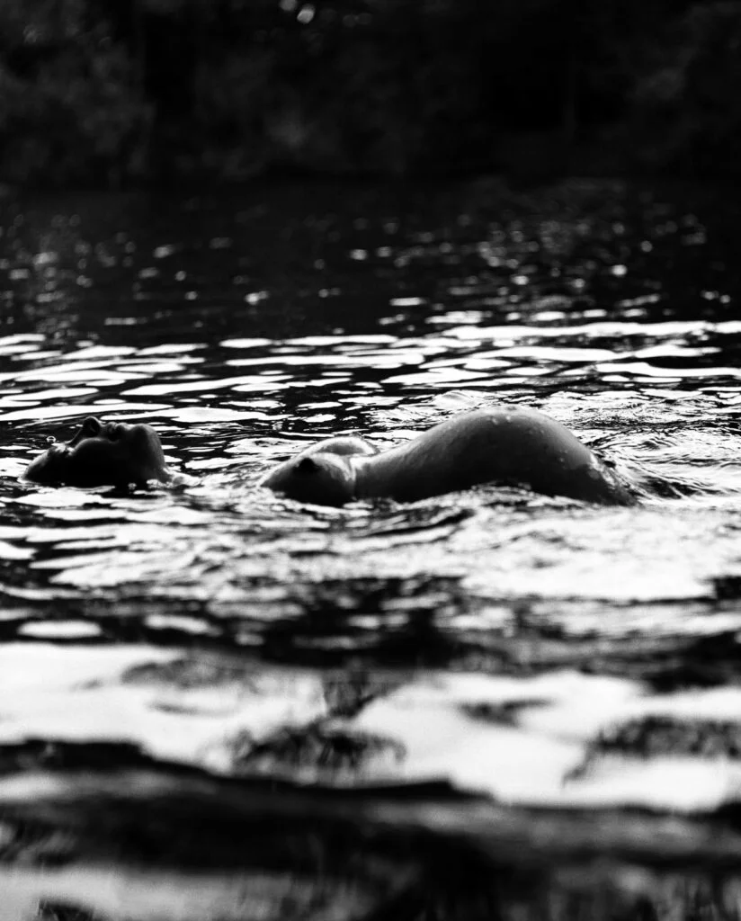 Schwangere schwimmt auf dem Rücken im See und hebt dabei ihren Babybauch aus dem Wasser bei den Babybauchfotos in Hamburg in der Natur