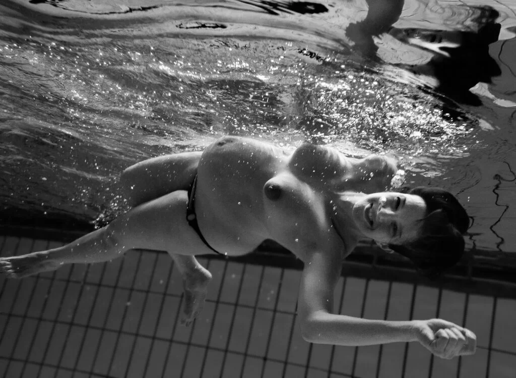 Schwangere taucht im Schwimmbecken und lacht dabei bei den Babybauchfotos in Hamburg Billstedt