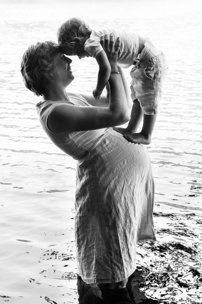 Mutter steht im Wasser mit ihrem Kind auf dem Arm bei den Babybauchfotos in Hamburg am See in der Natur