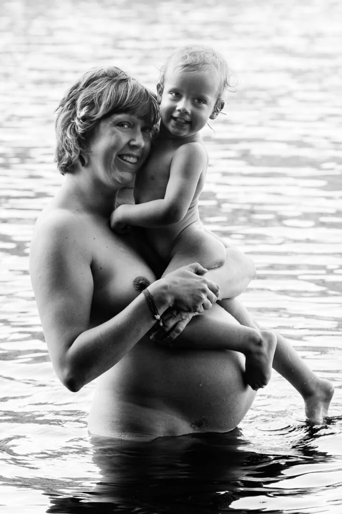 Mutter steht im Wasser mit ihrem Kind auf dem Arm bei den Babybauchfotos in Hamburg am See in der Natur
