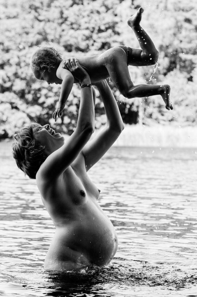 Mama steht im Wasser und hebt ihr Kind mit Schwung hoch in die Luft bei den Babybauchfotos in Hamburg am See
