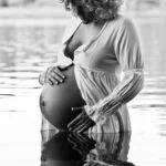 Mama steht im Wasser vom See mit ihren Händen anm Babybauch bei den Babybauchfotos in Hamburg outdoor in der Natur