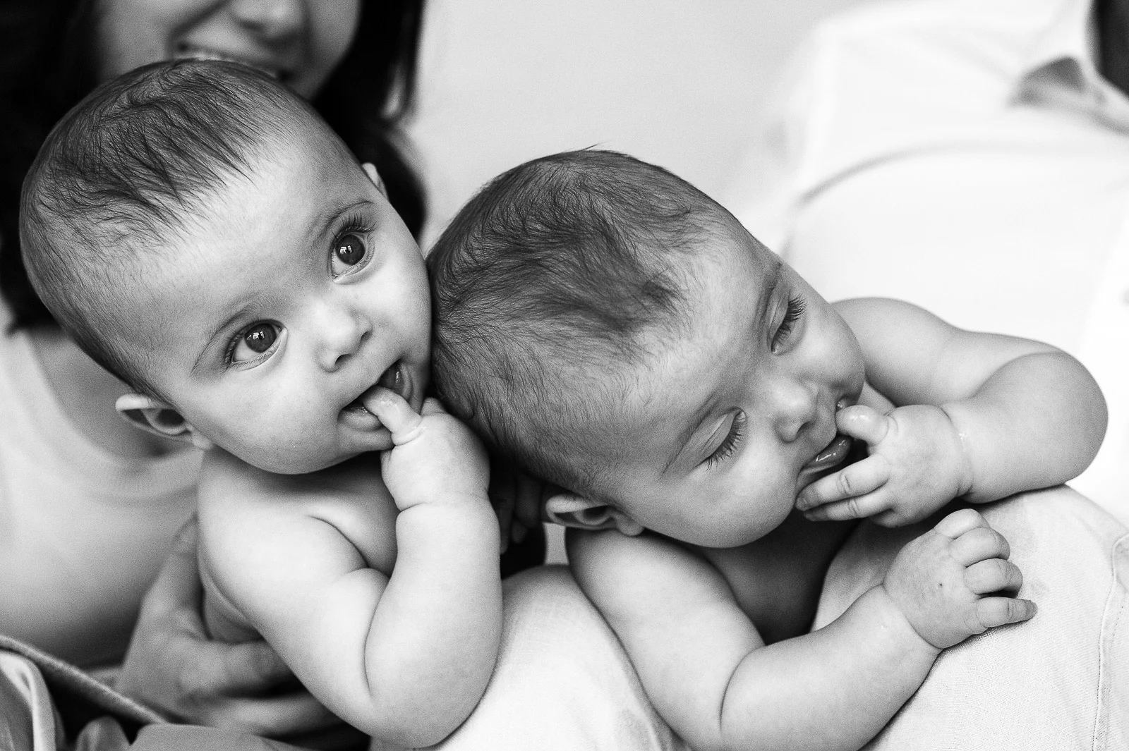 Baby Zwillinge nebeneinander auf dem Bauch liegend mit dem Finger im Mund beim Baby Fotoshooting in Hamburg Rotherbaum