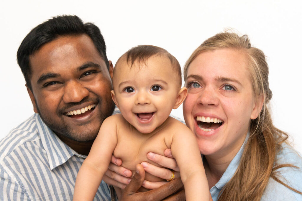 Mama und Papa kuscheln mit ihrem Baby und lachen in die Kamera beim Baby Fotoshooting und bei der Babyfotografie zuhause in Hamburg Poppenbüttel